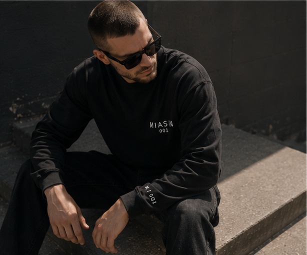 A model seated on a curb wearing the black MIASIN 001 long sleeve