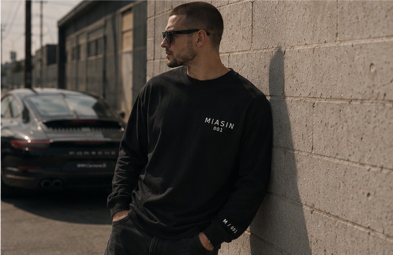 A model wearing the black MIASIN 001 long sleeve leaning against a block wall in Los Angeles