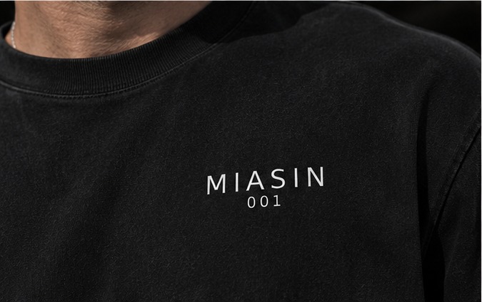 Close detail of the small MIASIN 001 chest mark on the black Box Tee